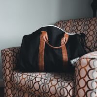 Juodas kelioninis krepšys su rudomis rankenomis ant sofos